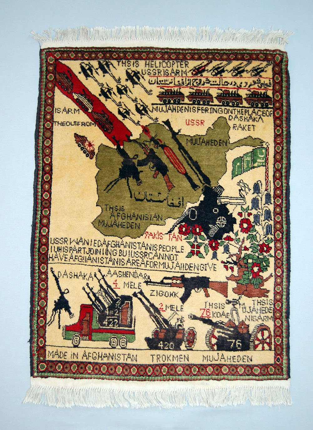 Also known as an “Exit,” “Protest,” or “Mujahideen” rug, this Afghan war rug depicts the withdrawal of Soviet forces from Afghanistan. On the rug’s lower third: types of anti-aircraft guns, including a “DASHAKA,” a 12.7mm M1938 DshKM heavy machine gun, and “ZIGORK,” a 14.5 ZGU-1 air defence weapon, 1989-2000. Textile, wool and cotton, 94 x 63 cm. © The Trustees of the British Museum.
